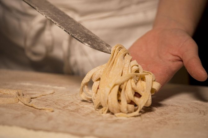 Hands cutting fresh tagliatelle on a floured wooden board